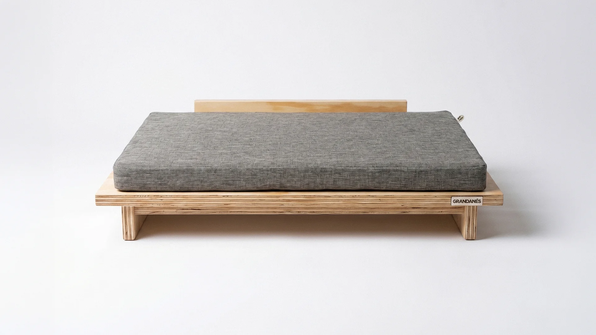 The Vetra bed in phenolic plywood with a gray cushion, on white.