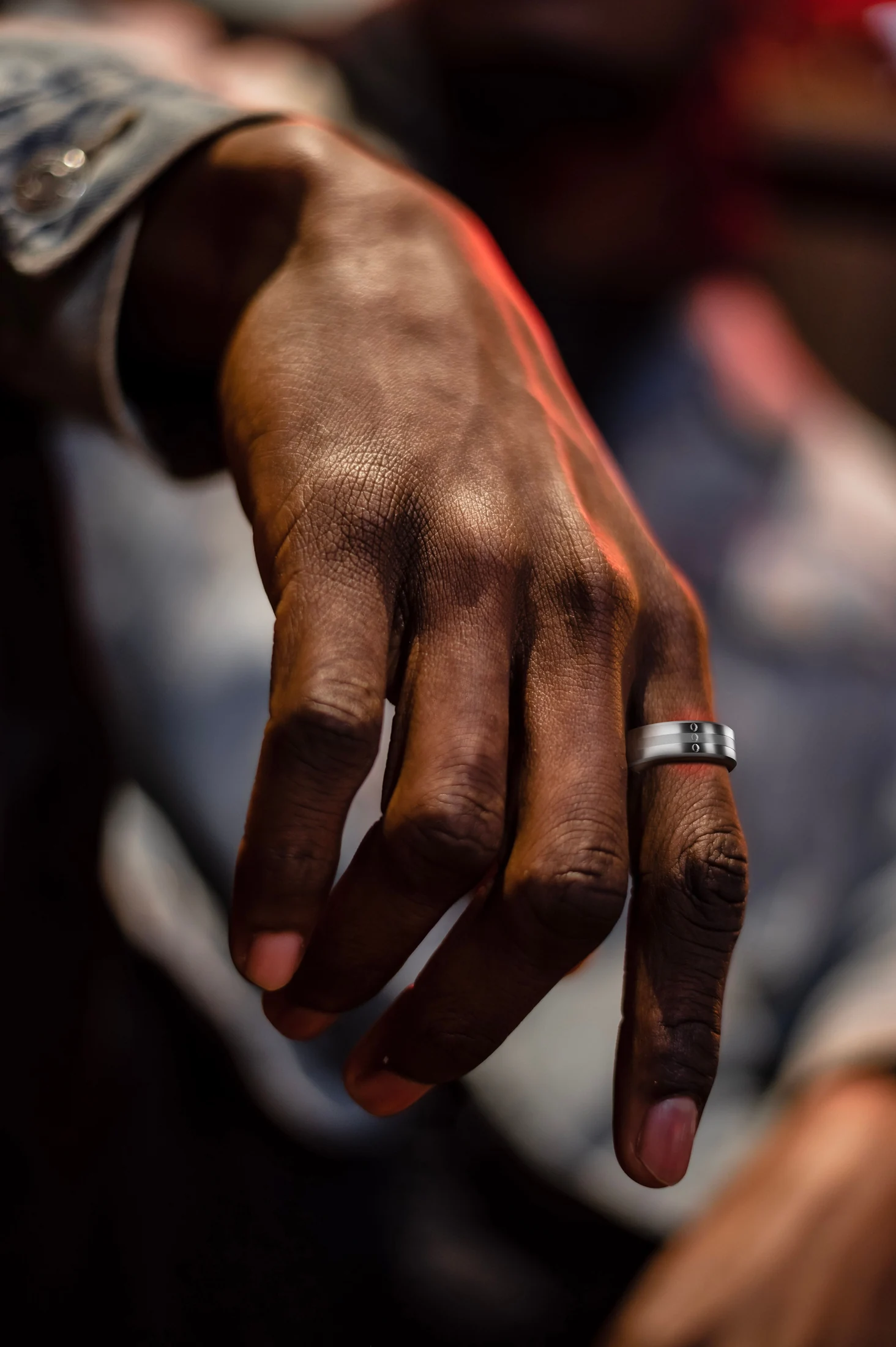 A hand wearing the Signal ring, with a denim sleeve, in warm low light.